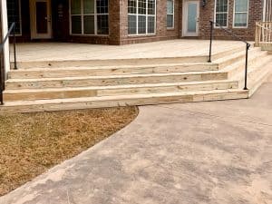 A detailed wooden deck with stairs and a concrete pathway in a residential backyard.