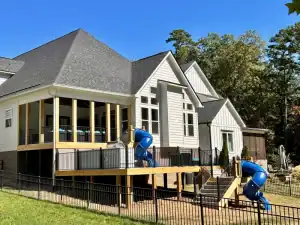 A vibrant backyard with a custom multi-level deck and two blue slides, surrounded by lush trees.