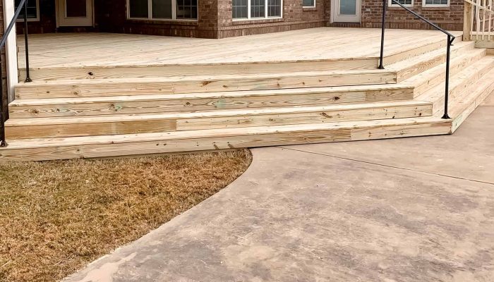 A detailed wooden deck with stairs and a concrete pathway in a residential backyard.