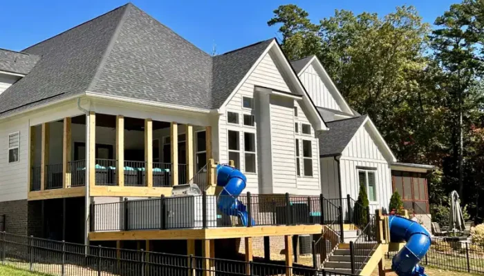 A vibrant backyard with a custom multi-level deck and two blue slides, surrounded by lush trees.